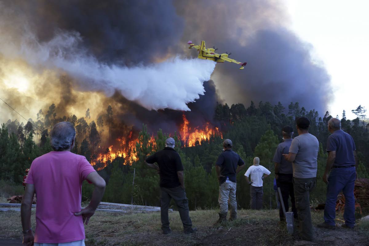 Villagers watch a firefighting plane drop water to stop a raging forest fire reaching their houses in Portugal.