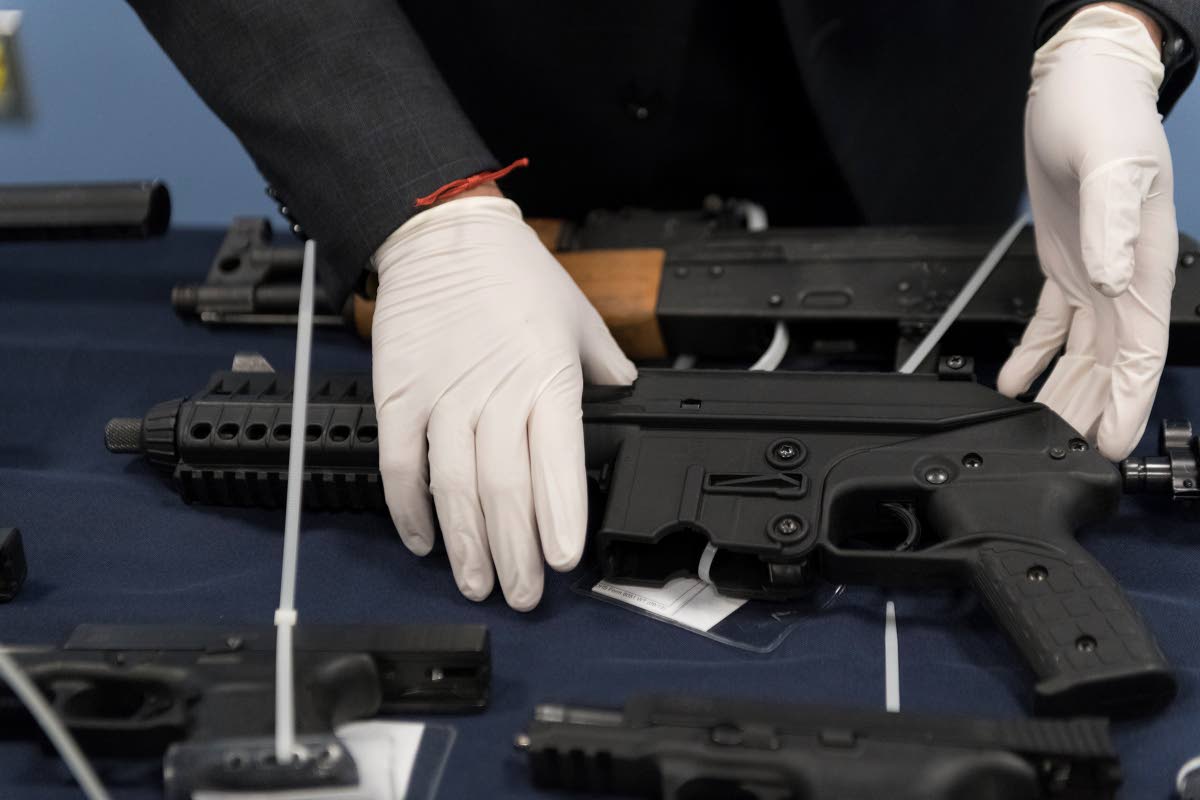 An agent of Homeland Security Investigations (HSI) handles one of more than 100 firearms seized in Miami in 2017, stopping the high-powered firearms and various others from reaching its planned destination of Kingston, Jamaica.