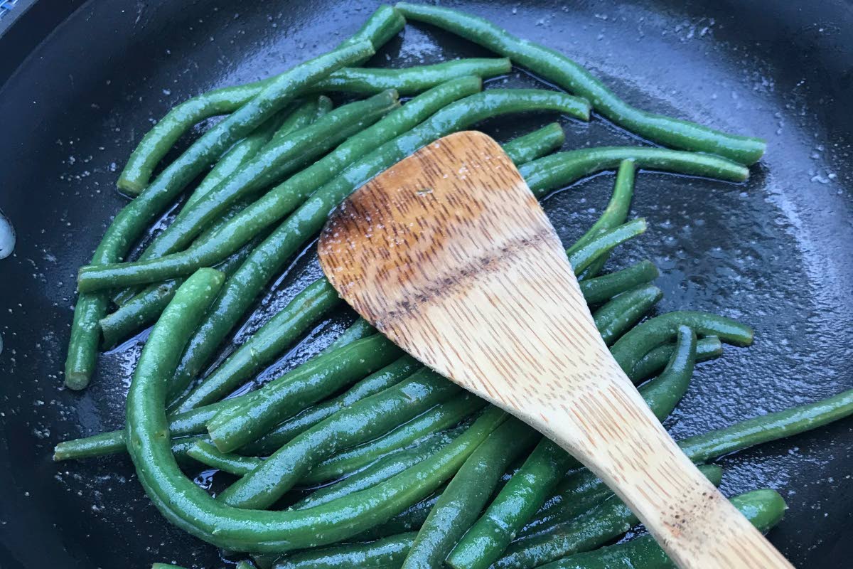 A plate of green beans picked from a home garden is prepared in a sauté pan.