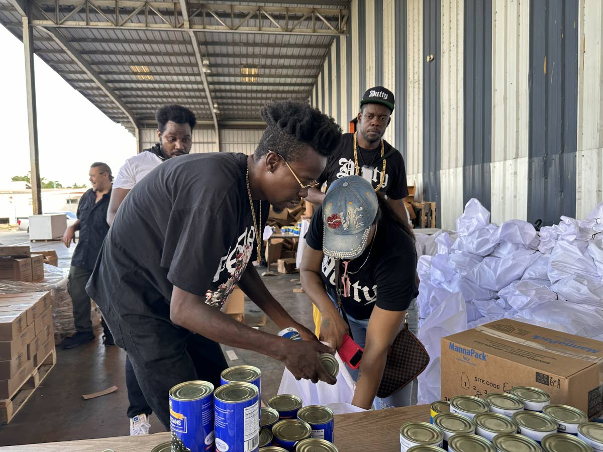 Dutty Rock Productions recording artistes Chi Ching Ching (left) and Goody Plum pack relief care packages during a visit to the Food For The Poor Jamaica headquarters in Spanish Town. 