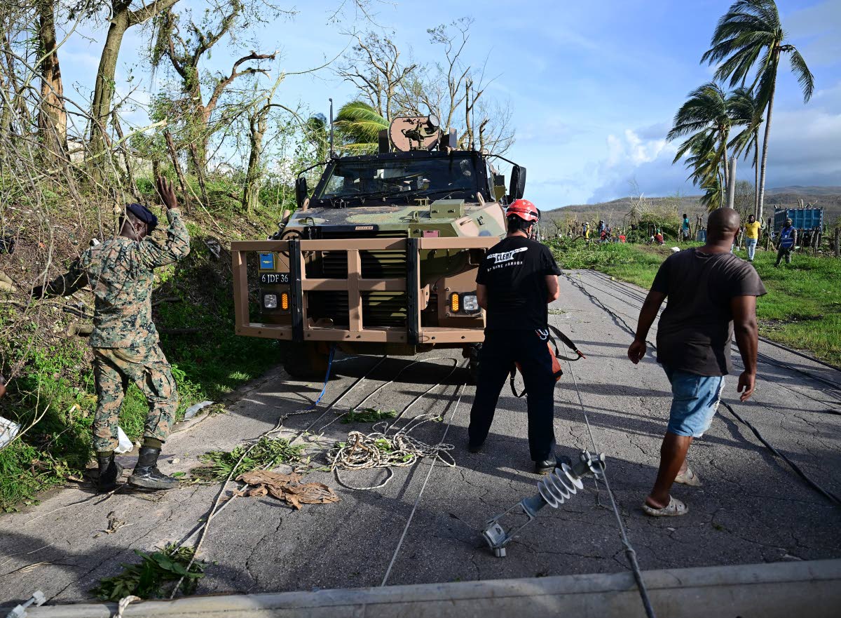 Members of the Jamaica Defence Force, aided by a volunteer from Australia, pull a downed concrete power pole from the roadway on October 29, after the passage of Hurricane Melissa. 