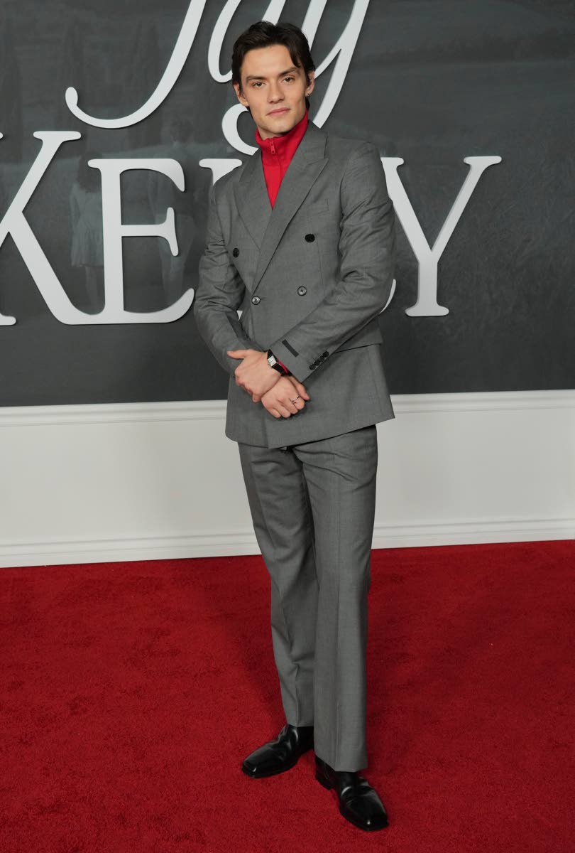 Louis Partridge pairs his grey double-breasted suit with a red polo neck shirt. 