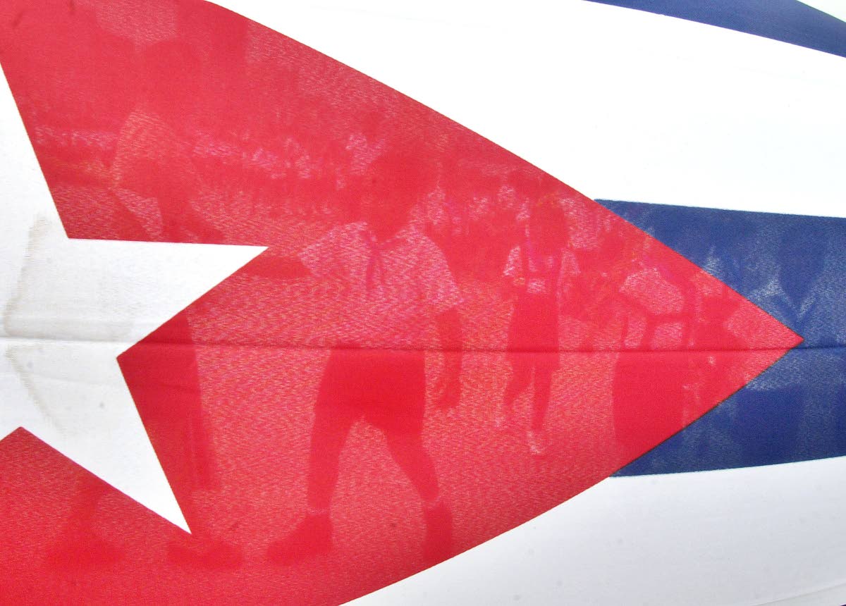Children are seen through the Cuban flag while they walk to the Havana's Malecon to toss flowers into the ocean in commemoration of the anniversary of the death of the Cuban revolutionary Commander Camilo Cienfuegos on October 28, 2004 in Havana, Cuba. (AP