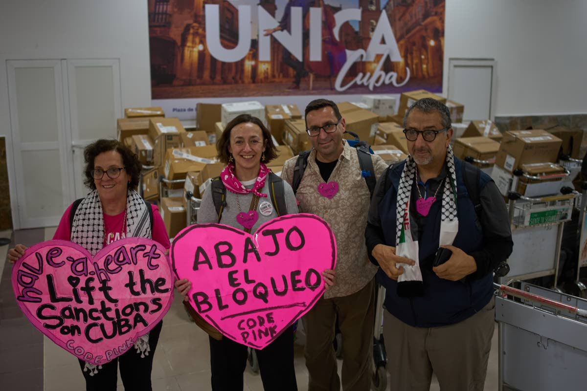 CODEPINK activists hold signs in front of boxes of aid they brought as part of the "Nuestra America," or Our America Convoy, after landing at the airport in Havana, Cuba, Friday, March 20, 2026.