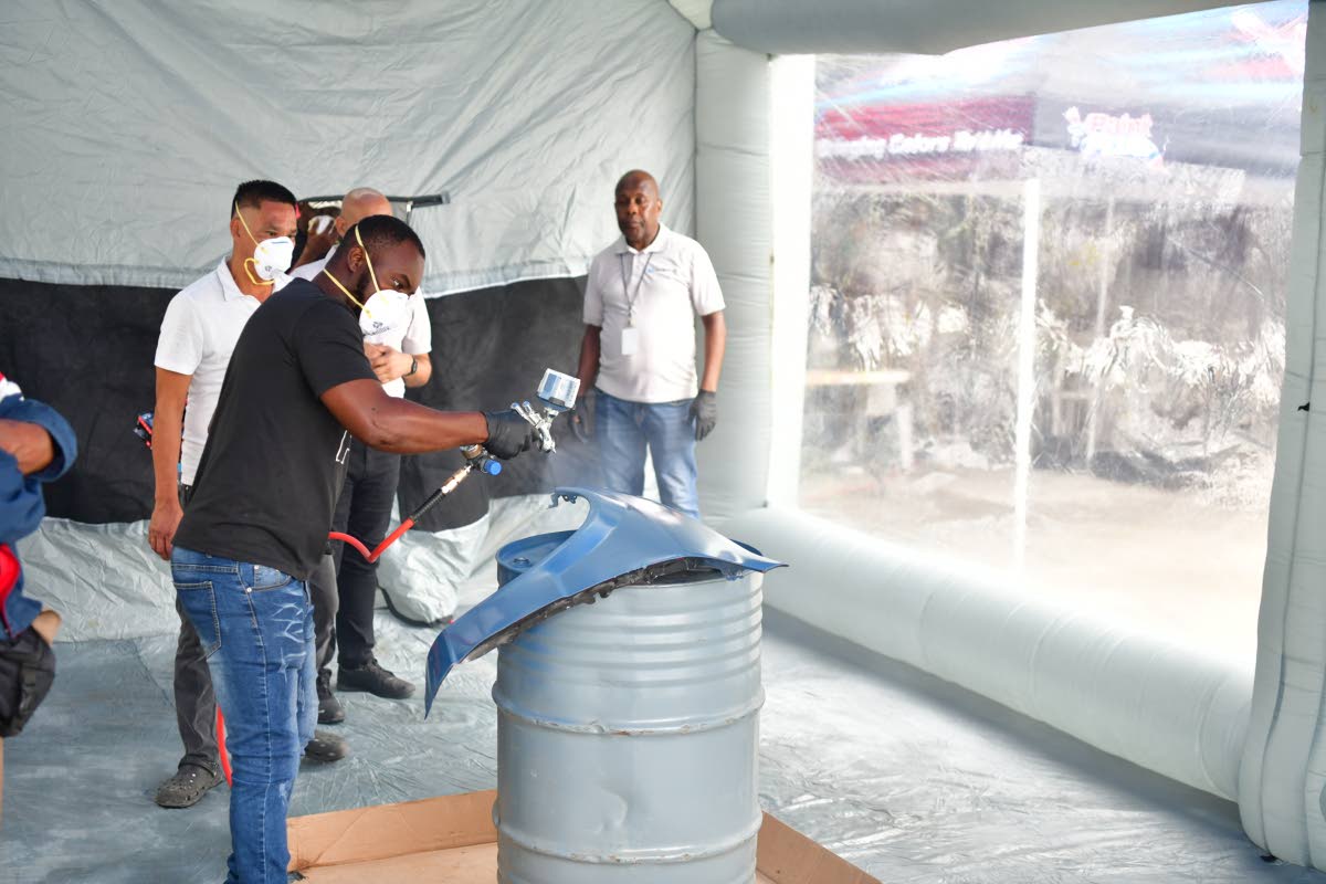  Chanderpaul Powell, an automotive painter, participates in the demonstration by applying paint to a fender at the Berger Paints Jamaica Automotive Seminar in Montego Bay, St James. Looking on are Ande Lee, garage manager for Westron Ltd, and Alton McCalla