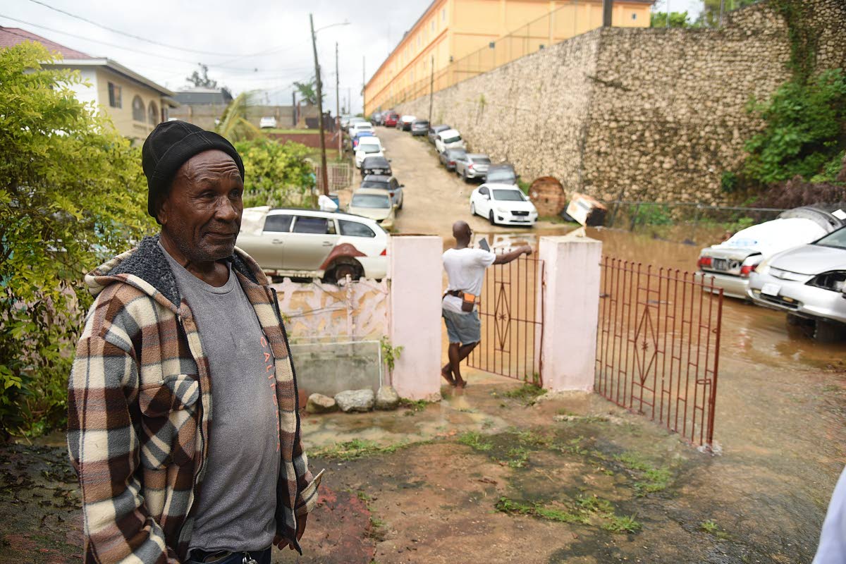 Leebert Campbell, resident of  Gibson Close in Mandeville, watches as water flows through his yard during a heavy downpour last week.