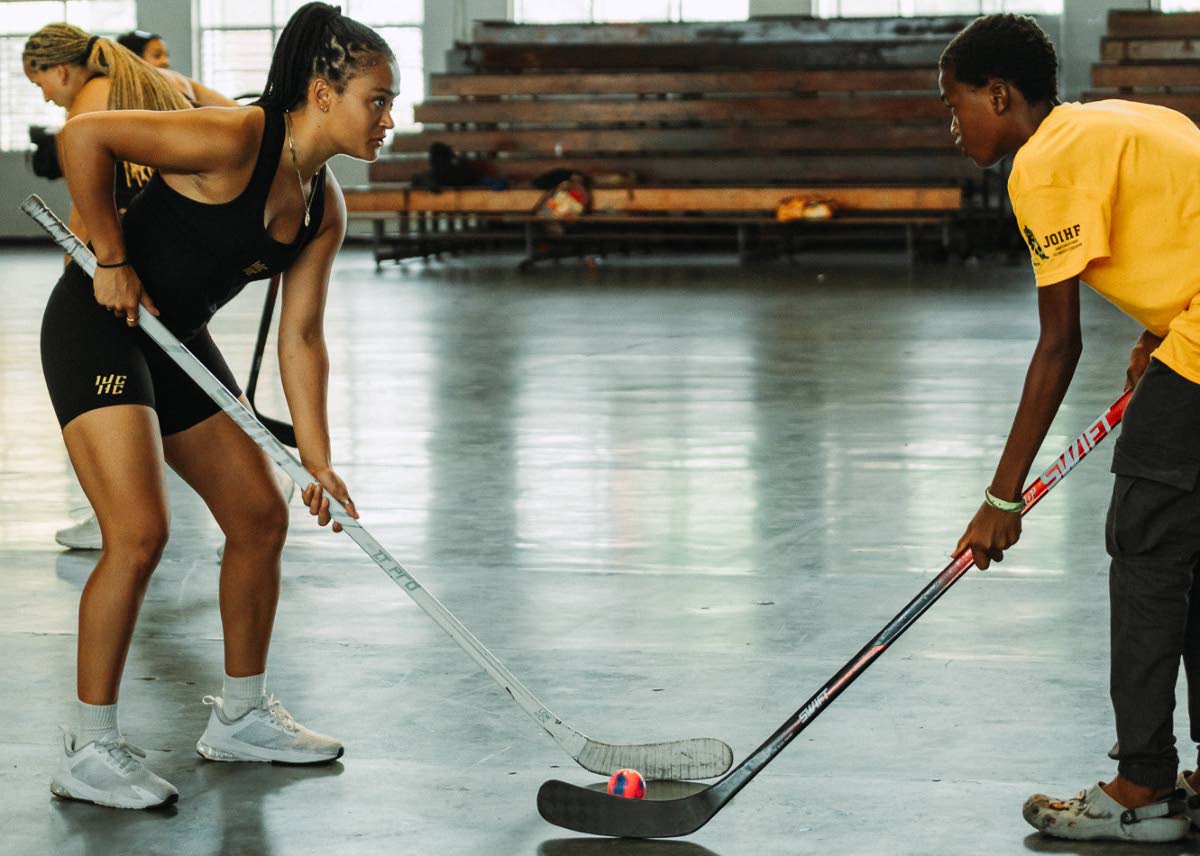 
This image provided by the Women of Colour Hockey Collective shows Dartmouth College player Dayton O’Donoghue (left) and preparing for a faceoff with a participant during a hockey clinic inside the Jamaican National Stadium in Kingston, Jamaica, Saturda