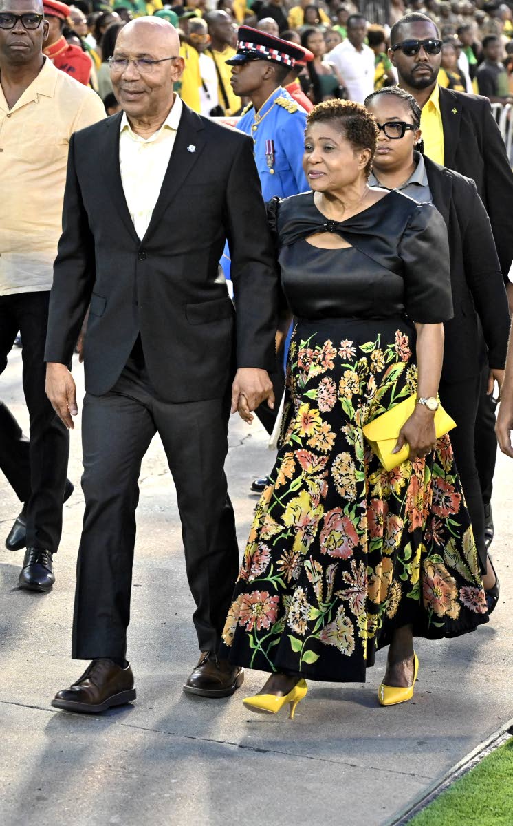 Sir Patrick Allen and Lady Allen arrive at the Grand Gala at the National Stadium, with Sir Patrick in a black suit and Lady Allen in florals accented with yellow accessories.