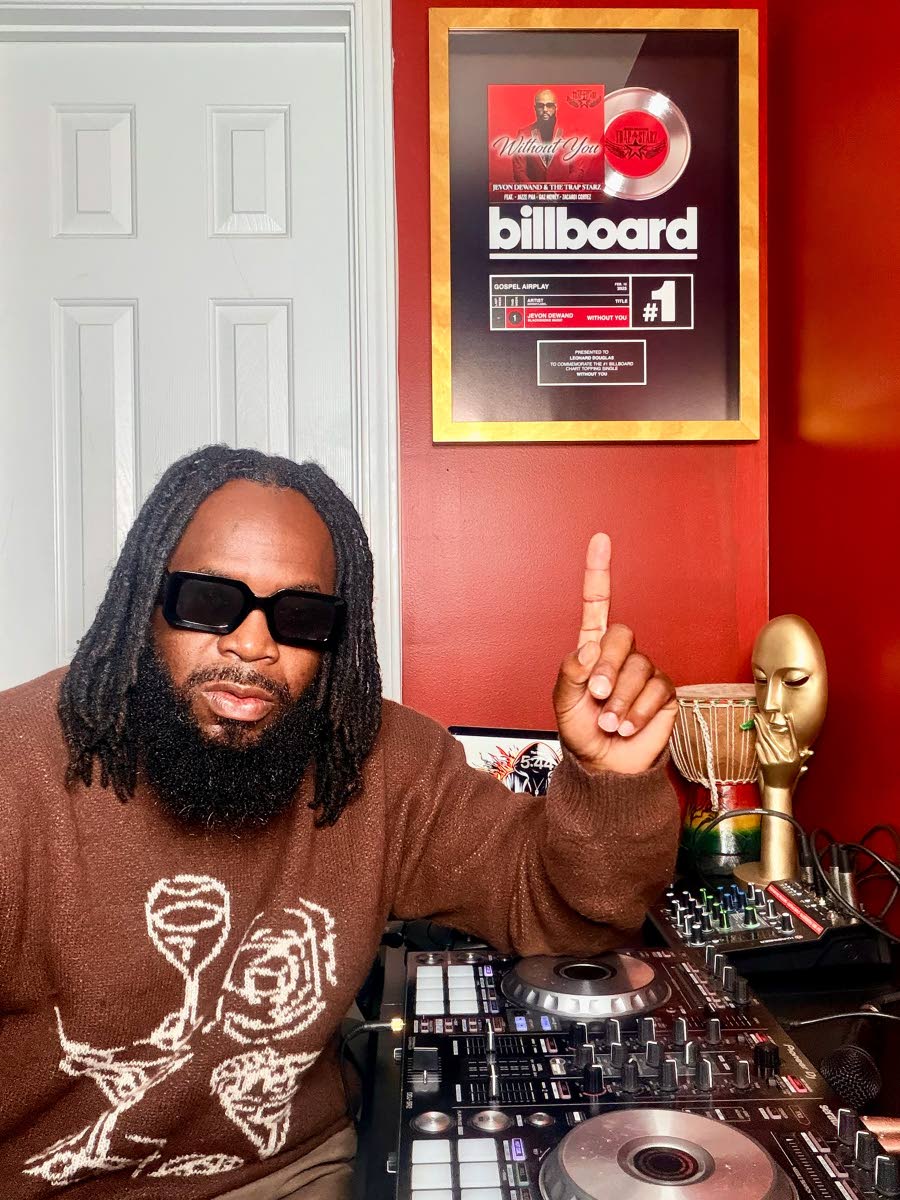 DJ Damage sits in front of his Billboard No. 1 plaque hanging prominently on the wall.