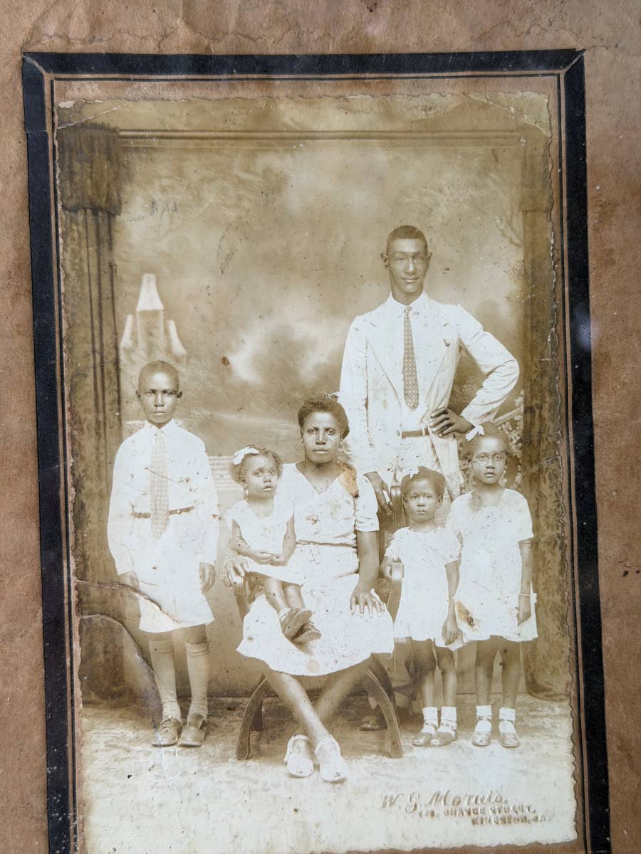A framed, faded photograph featuring Edna’s father, Aston Lindsay; her mother, Idaline Lindsay; and four young children, a boy, Horace, and three girls, Rosie, Beezy and Monica. 