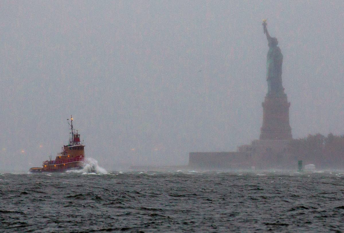 Waves crash over the bow of a tug boat as it passes near the Statue of Liberty in New York as rough water as the result of Hurricane Sandy churns the waters of New York Harbour in October 2012.