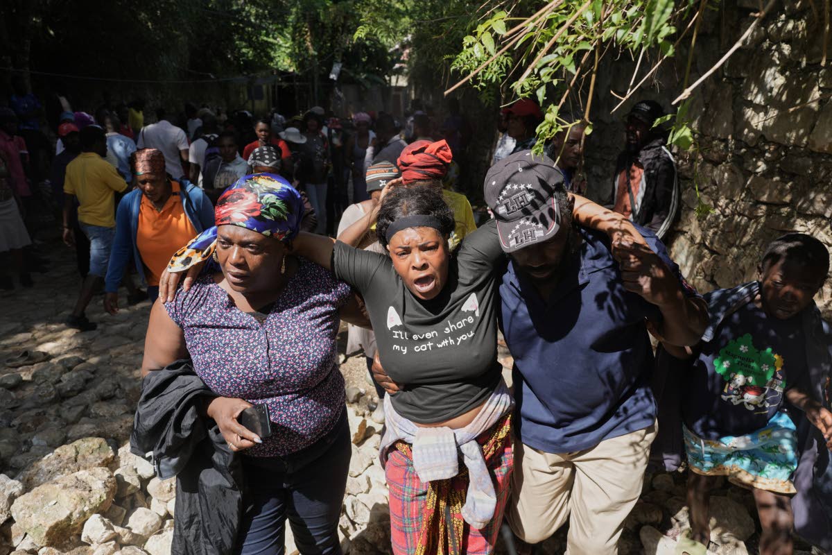 People watch as the bodies of their relatives who were killed in a gang attack are carried away by morgue workers in the Kenscoff neighborhood of Port-au-Prince, Haiti, Monday, Aug. 24, 2026. (AP Photo/Odelyn Joseph)