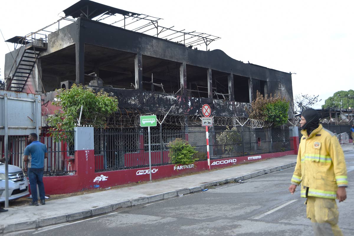A fireman walks past the burnt out Superior Parts building along Hagley Park Road in St Andrew on Friday.