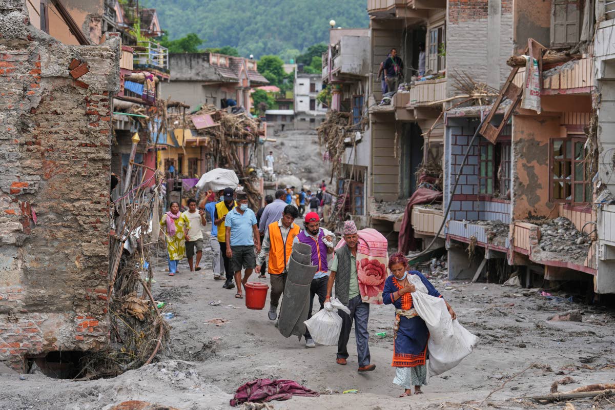 Residents carry their belongings salvaged from their damaged homes filled with mud and debris in Devighat, in Nepal’s Nuwakot district, following the flash floods.