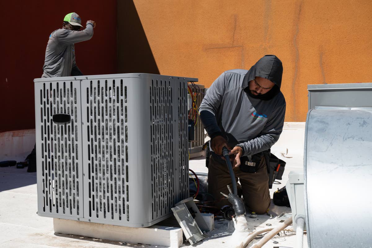 Sonel Telemaque (left) wipes sweat from his brow while installing a new air conditioning unit alongside Brian Hermosillo during record-breaking heat on March 19 in Tempe, Arizona.