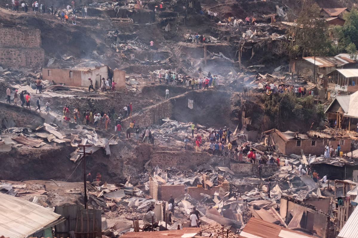 People walk amid the charred remains of homes near a primary school and a secondary school where a fire broke out, killing several students, in Bukavu, Congo, Thursday, Sept. 10, 2026. (AP Photo/Janvier Barhahiga)