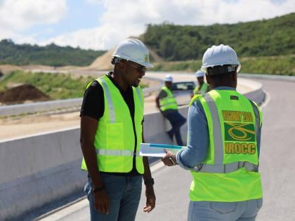Robert Morgan (left), minister without portfolio in the Ministry of Economic, Growth and Job Creation with responsibility for works, examines documents related to the Montego Bay Perimeter Road, now under construction, during a tour of the construction sit