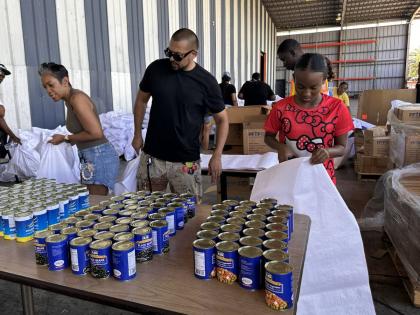 International recording artiste Sean Paul (centre), his sister-in-law Winsome Henriques (left), and a volunteer of the Sean Paul Foundation, Alana Thomas, get ready to  package food items during their visit to the Food For The Poor Jamaica. 
