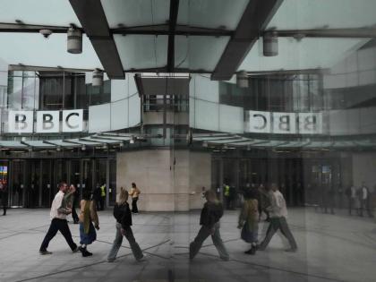 Pedestrians are reflected as they walk outside BBC Broadcasting House in London, Tuesday, November 11, 2025. (AP Photo/Kirsty Wigglesworth, file)