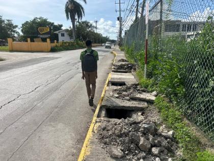 The crumbling sidewalk in front of the National Works Agency office along Barracks Road in Savanna-la-Mar, Westmoreland, forces this student to walk on the road surface.