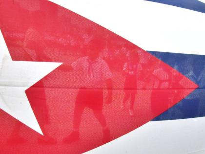 Children are seen through the Cuban flag while they walk to the Havana's Malecon to toss flowers into the ocean in commemoration of the anniversary of the death of the Cuban revolutionary Commander Camilo Cienfuegos on October 28, 2004 in Havana, Cuba. (AP