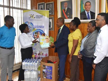 Jamaica Information Service (JIS) Director of Human Resources Management and Development, Dr. David Knight (third left) hands over a package of baby diapers to Jamaica Network of Rural Women Producers Executive Board Member, Marva Allen-Simms, which is par