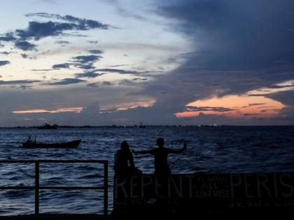 People sit on the seawall as the sun sets in Georgetown, Guyana.