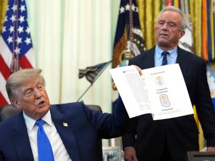 President Donald Trump holds up an image taken from his Truth Social account as Health and Human Services Secretary Robert F. Kennedy Jr. watches during a meeting to sign an executive order about vaccines, Monday, Aug. 10, 2026, in the Oval Office of the W