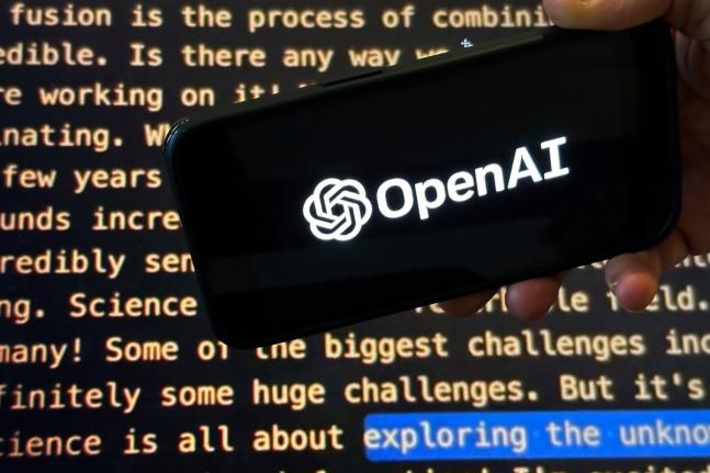 The OpenAI logo appears on a mobile phone in front of a screen showing part of the company website in this photo taken on November 21, 2023 in New York. (AP Photo/Peter Morgan, File)