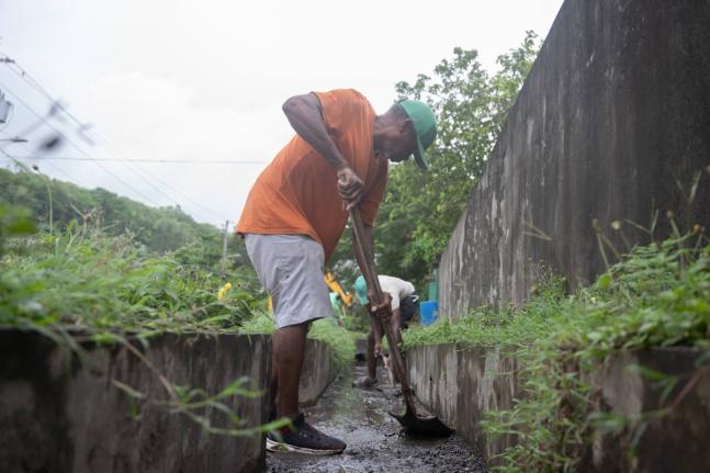 Workmen labour to clear debris from drains along the Race Course main road in St Mary on Monday.