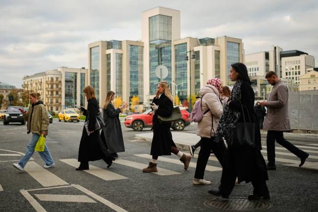 People cross a street, with Russian oil company Lukoil’s headquarters seen in the background, in Moscow, Russia, on Thursday, October, 23, 2025.
