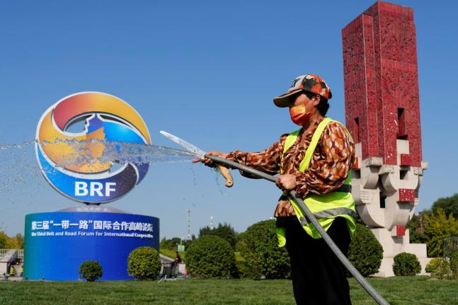 A gardener waters the grass near the logo for the Belt and Road Forum in Beijing, Monday, October 16, 2023. China’s Belt and Road Initiative looks to become smaller and greener after a decade of big projects that boosted trade but left big debts and rais