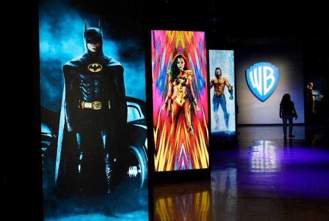 In this June 24, 2021, photo, a visitor walks past portraits of DC Comics superheroes as she enters the ‘Action and Magic Made Here’ interactive experience at the Warner Bros Studio Tour Hollywood media preview in Burbank, California.