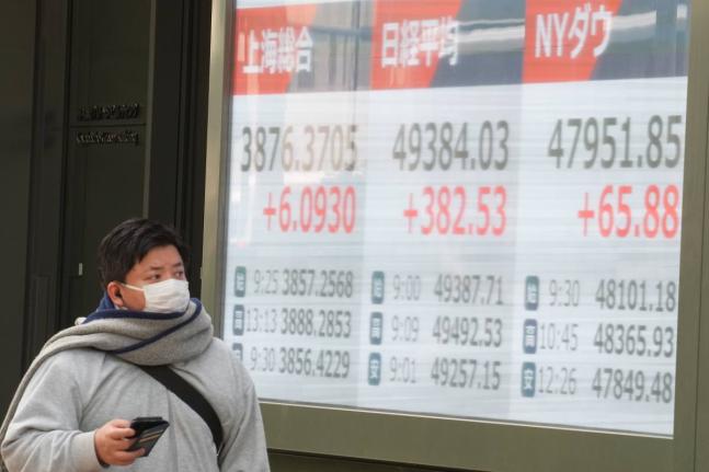 
A person walks in front of an electronic stock board showing the market indexes of Shanghai, Tokyo and New York Dow at a securities firm in Tokyo, Japan. 