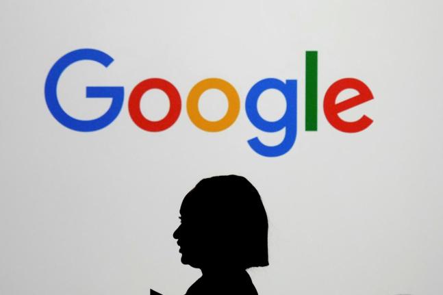 A woman walks by a giant screen with a logo at an event at the Paris Google Lab on the sidelines of the AI Action Summit in Paris on February 9, 2025. 