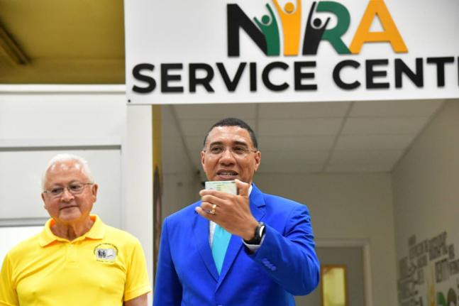 Prime Minister, Dr Andrew Holness (right), displays his national identification card during the official launch of the National Identification Registration Authority (NIRA) at the NIRA Centre, Central Sorting Office in Kingston. Looking on is Minister of J