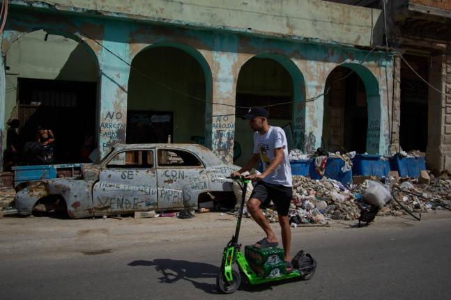 A man rides a scooter past a wrecked car and garbage during a blackout in Havana.