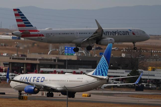 An American Airlines jetliner lands on a runway as a United Airlines plane waits for clearance to take off as high winds strafe Denver International Airport Thursday, March 12, 2026, in Denver. (AP Photo/David Zalubowski)