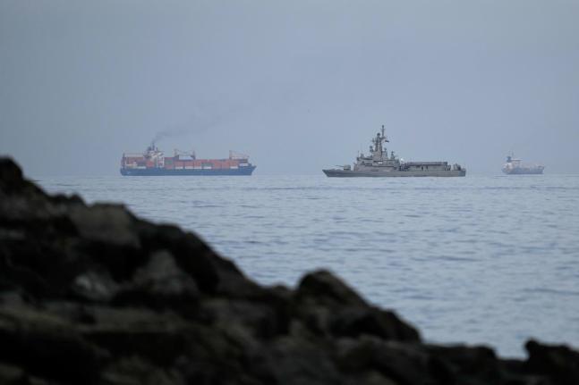 A UAE navy ship sails next to a cargo ship in the Strait of Hormuz, as seen from Khor Fakkan, United Arab Emirates.