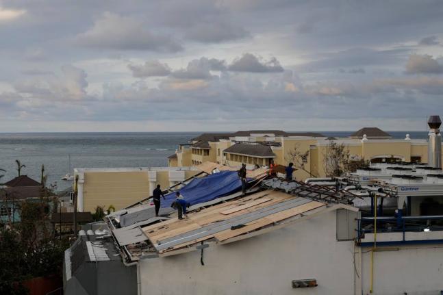 In this October 31, 2025, photo people are seen repairing the roof of a resort in Montego Bay, Jamaica, in the aftermath of Hurricane Melissa.