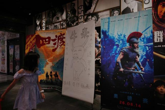 A man girl walks by a drawing poster promoting a Chinese animated film ‘Niu Lai’ on display with other movie posters at a cinema in Beijing on Tuesday.