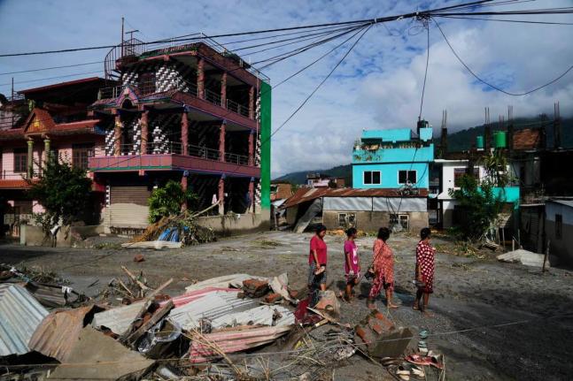 People walk past damage in the aftermath of flash floods in Devighat in the Nuwakot district in Nepal on Thursday. - AP photo
