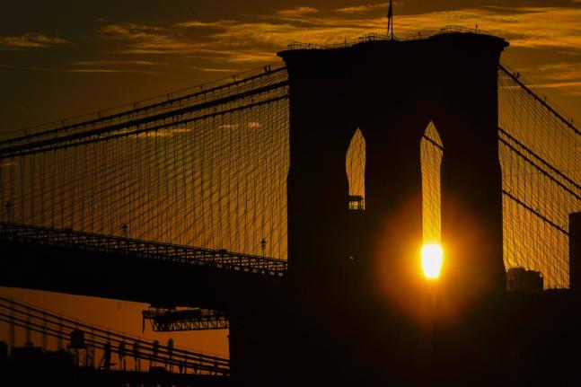 FILE - The sun rises behind the Brooklyn Bridge on Oct. 11, 2023, in New York. (AP Photo/Kiichiro Sato, File)