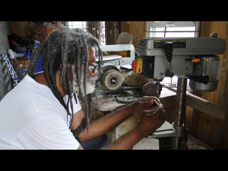 Ras Mel piercing a pendant in his workshop.