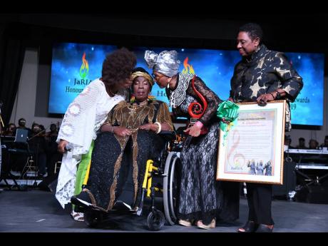 Credit: Rudolph Brown Rita Marley (seated) receives a kiss from fellow members of the I-Three, Judy Mowatt (left) and Marcia Griffiths (second right), while Minister of Culture, Gender, Entertainment and Sports Olivia ‘Babsy’ Grange looks on. Occasion was the Reggae 50 Awards during February’s Reggae Month celebrations.