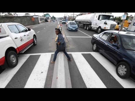 Sixty-one-year-old Arleen Byrd steps over a Jersey barrier as she uses a pedestrian crossing along the busy Constant Spring Road in St Andrew yesterday.