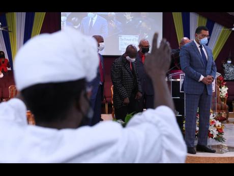 With hands outstretched, a worshipper joins Prime Minister Andrew Holness and clerics in prayer on the rostrum during a National Day of Prayer held at the Power of Faith Minitries church in Portmore, St Catherine, on Wednesday. 