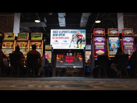 This file photo shows a huge TV screen at the entrance of Churchill’s Bourbon & Brew Bar & Grille, flanked by electronic gaming machines, promotes sports betting at Turfway Park Racing & Gaming on December 22, 2023, in Florence, Kentucky. A bill that wou