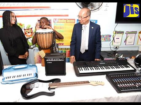 Credit: Contributed National Security Minister Dr Horace Chang (right) and Acting Vice-Principal, Kingston High School, Sashauna Gordon (left), look on as grade-seven student Kimani Davis shows off his drumming skills. The event was the handover of musical instruments, value