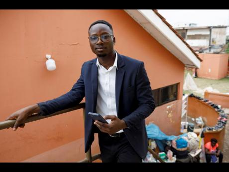 Shadrach Damateye, a co-founder of Masters Hive Centre for Innovation, who uses his mobile phone to help business owners, poses for a photograph outside his office in Tema, Ghana, Tuesday, April 23, 2024.